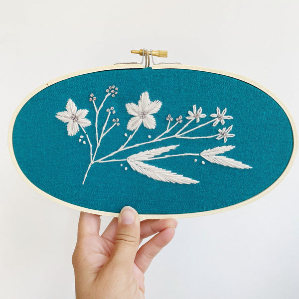 White floral embroidery on dark teal linen fabric